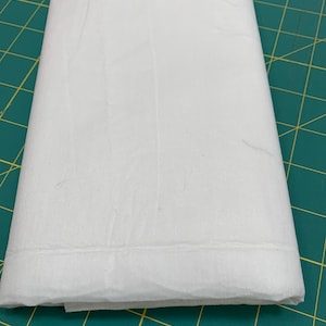 May include: A white, folded piece of fabric on a green cutting mat.