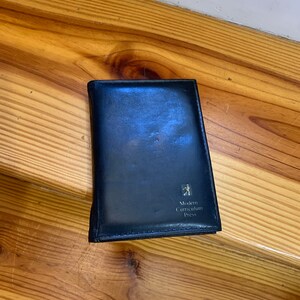 May include: A black leather book with the text "Modern Curriculum Press" and a logo. The book is closed and appears to be sitting on a wooden surface. The book's cover is slightly worn.