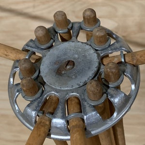May include: An antique wooden clothes drying rack with a metal center. The rack has a circular metal piece with wooden pegs and arms extending outwards. The metal piece has text on it. The wooden arms are attached to the metal piece with metal rings.