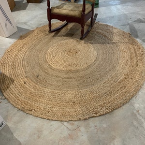 May include: A round, natural fiber rug with a woven design. The rug is light brown and has a circular shape. It is made of natural materials and has a rustic look.