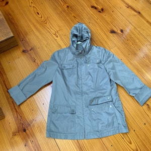 May include: A light gray hooded jacket with a zipper closure and two pockets. The jacket has a relaxed fit and a casual style.