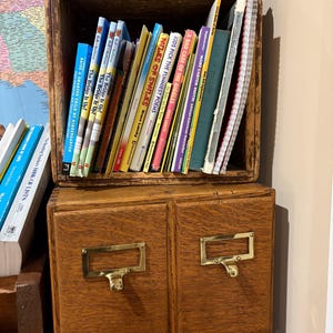 May include: A wooden box with two drawers and brass pulls. The box is filled with a variety of children's books, including "Miles of Smiles" and "A Bad Case of the Giggles".