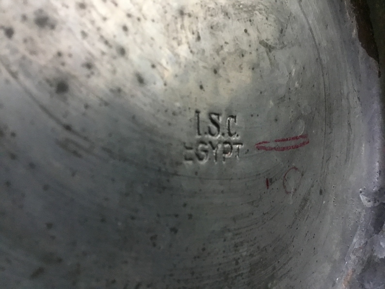 K&ouml;nnte beinhalten: Nahaufnahme einer metallischen Oberfl&auml;che mit dem eingestempelten Text "I.S.C. EGYPT". Das Metall hat ein abgenutztes, strukturiertes Aussehen mit sichtbaren Kratzern und Unvollkommenheiten. Eine rote Markierung ist vorhanden.