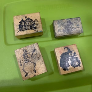 May include: Four wooden stamps with Halloween themes. The stamps feature a haunted house, a skeleton, a witch, and a blank stamp.
