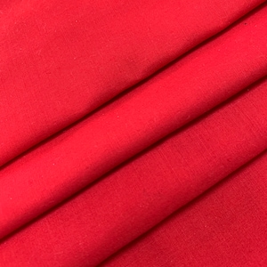 May include: Close-up of a vibrant red fabric with visible texture. The fabric is folded in diagonal layers, creating shadows and highlighting the material's texture. The color is consistent throughout the image.