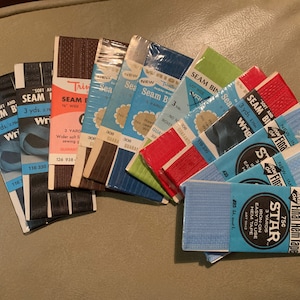 May include: A collection of vintage seam binding tape in various colors, including blue, red, brown, and green. The tape is packaged in small cardboard boxes with the brand name "Wright's" and "Star" printed on them. The boxes also indicate the length of the tape, which is 3 yards.