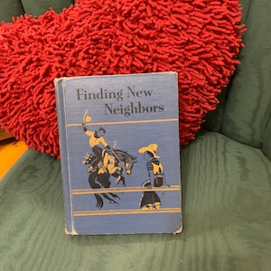 May include: A blue book with the title "Finding New Neighbors" on the cover. The cover features a black and white illustration of two boys, one riding a horse and the other standing nearby.