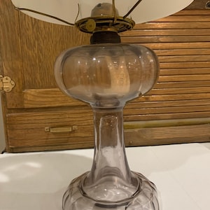May include: A vintage oil lamp with a clear glass base and a frosted glass shade. The lamp has a bulbous body and a slender neck, with a metal fixture holding the shade. The lamp is likely from the early 20th century.
