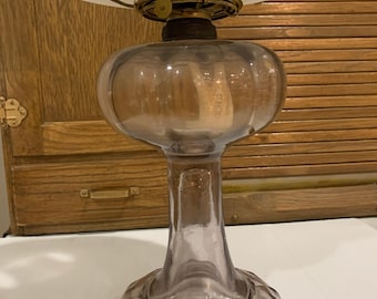 May include: A vintage oil lamp with a clear glass base and a frosted glass shade. The lamp has a bulbous body and a slender neck, with a metal fixture holding the shade. The lamp is likely from the early 20th century.