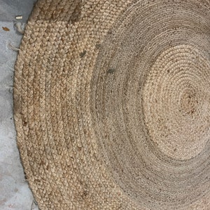 May include: A round, natural fiber rug with a woven texture. The rug is made of jute and has a light brown color.