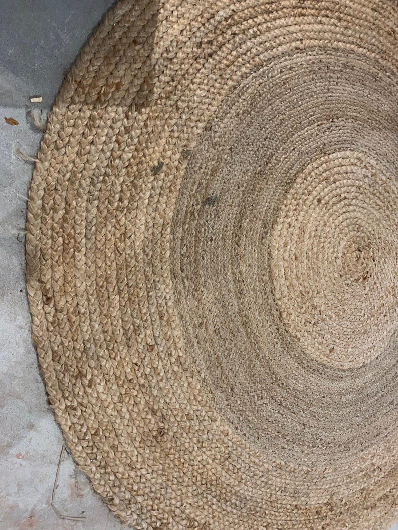 May include: A round, natural fiber rug with a woven texture. The rug is made of jute and has a light brown color.