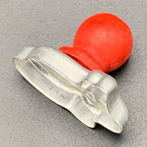 May include: A silver metal cookie cutter shaped like a Christmas tree with a red wooden knob on top.