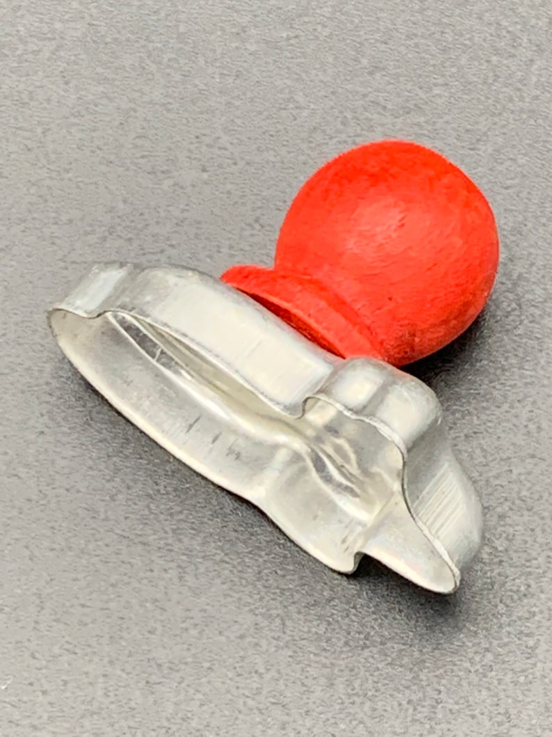May include: A silver metal cookie cutter shaped like a Christmas tree with a red wooden knob on top.