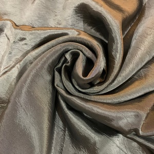 May include: A close-up of a crumpled piece of fabric with a shimmery, metallic finish. The fabric is a dark brown color with a subtle sheen.