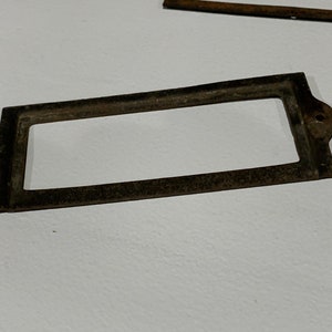 May include: A rusty metal label holder with rounded corners and two small holes on the top.