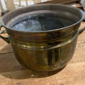 May include: A brass planter with two handles. The planter is round and has a slightly flared lip. It has a worn, aged look.