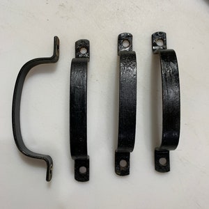 May include: Four black metal shelf brackets with two holes on each bracket. The brackets are curved and have a smooth finish.