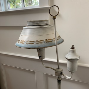 May include: A white floor lamp with a white and blue painted lampshade. The lampshade has a gold trim and a gold design. The lamp has a white metal base and a white metal arm.