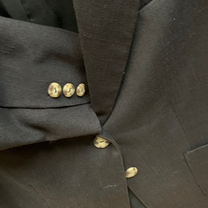 May include: A black blazer with a textured fabric and four brown buttons on the sleeve. The blazer has two pockets on the front.