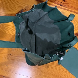Puede incluir: Vista abierta de un bolso tote verde azulado con una bolsa a juego. El bolso tote tiene dos asas y un cierre de cord&oacute;n. La bolsa tiene cierre de cremallera y una correa peque&ntilde;a. La bolsa est&aacute; hecha de un material suave.