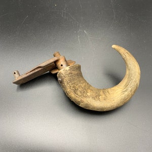 May include: A vintage, rustic door handle made from a curved piece of wood with a metal latch attached. The handle is brown and has a natural wood grain.