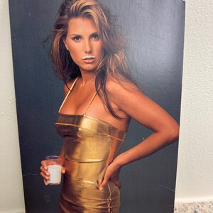 May include: A woman wearing a gold metallic dress and holding a glass of milk. She has a white mustache from the milk.