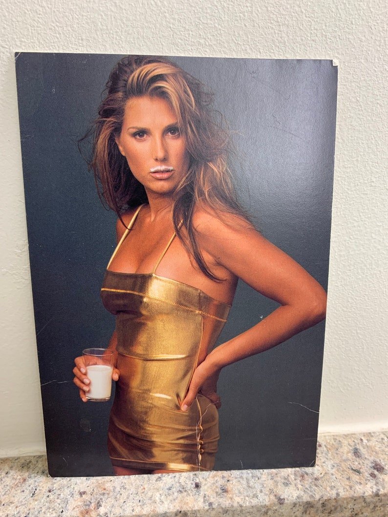 May include: A woman wearing a gold metallic dress and holding a glass of milk. She has a white mustache from the milk.