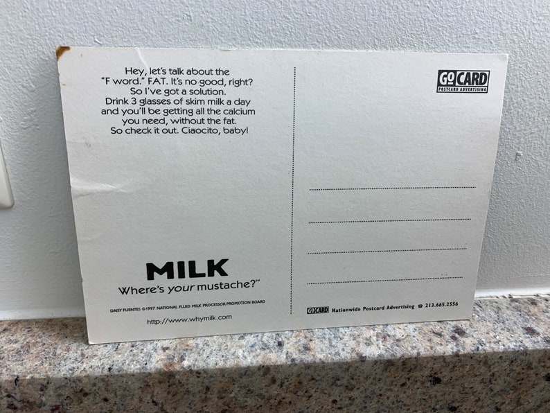 May include: A white postcard with black text promoting milk. The text reads "Hey, let's talk about the 'F word.' FAT. It's no good, right? So I've got a solution. Drink 3 glasses of skim milk a day and you'll be getting all the calcium you need, without the fat. So check it out. Ciaocito, baby!"  The bottom of the postcard reads "MILK Where's your mustache?" and "http://www.whymilk.com".