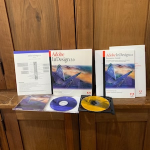 May include: Adobe InDesign 2.0 software package with a user guide, resource guide, and two CDs. The cover of the user guide features a colorful butterfly against a sunset background. The text "Adobe InDesign 2.0" is printed in red and white on the cover.