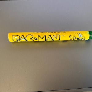 May include: Yellow and green Pac-Man pencil with the text "PAC-MAN" and "© 1983 Bally Midway Mfg. Co. TM" printed on it.