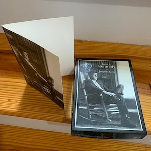 May include: A black and white photo of John F. Kennedy sitting in a rocking chair. The book is titled "John F. Kennedy" by Jacques Lowe.