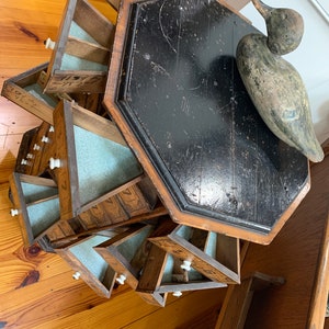 Puede incluir: Un mueble antiguo de madera con m&uacute;ltiples cajones peque&ntilde;os, cada uno con un pomo blanco. El mueble est&aacute; sujeto a un respaldo de madera negro octogonal. Un se&ntilde;uelo de pato de madera descansa sobre el respaldo.