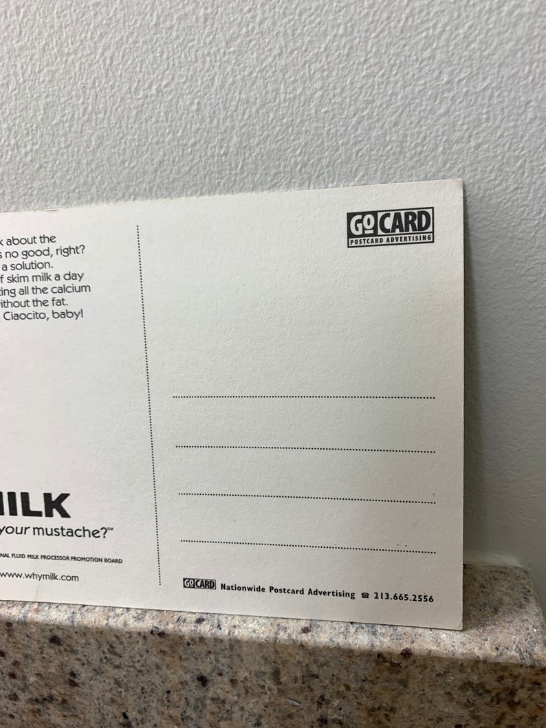 May include: A white postcard with a black and white illustration of a milk mustache. The text on the postcard reads "Milk your mustache?" and "Why Milk?" The postcard also includes the text "GoCard Nationwide Postcard Advertising 213.665.2556".