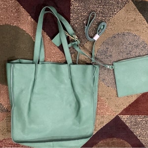Puede incluir: Un bolso tote de cuero verde menta con un bolso bandolera y una correa a juego. El bolso tote tiene dos asas y una etiqueta adjunta. Las bolsas est&aacute;n sobre una alfombra estampada marr&oacute;n, beige y burdeos.
