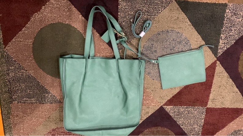Puede incluir: Un bolso tote de cuero verde menta con un bolso bandolera y una correa a juego. El bolso tote tiene dos asas y una etiqueta adjunta. Las bolsas est&aacute;n sobre una alfombra estampada marr&oacute;n, beige y burdeos.