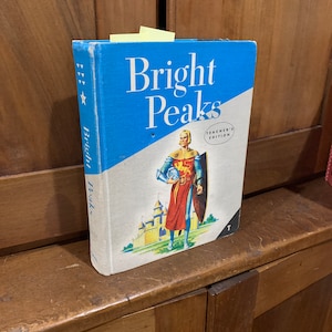 May include: A blue and white book titled "Bright Peaks" with a picture of a knight in armor standing in front of a castle. The book is a teacher's edition.