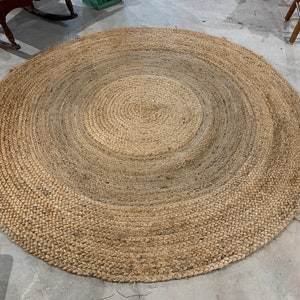 May include: A round, natural fiber rug with a woven design. The rug has a light brown color with a darker brown center.
