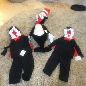 May include: Two black and red children's costumes of the Cat in the Hat, with a plush toy of the Cat in the Hat in the background.
