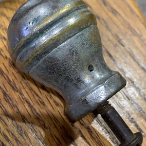May include: A silver-toned metal knob with a gold band around the top. The knob has a screw on the bottom.