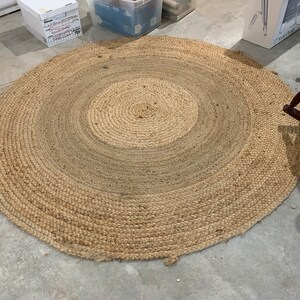 May include: A round, natural fiber rug with a woven design. The rug has a light brown color and a circular shape.