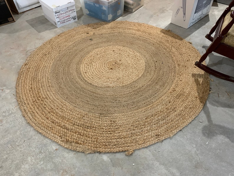 May include: A round, natural fiber rug with a woven design. The rug has a light brown color and a circular shape.
