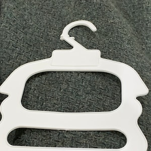 May include: White plastic hanger with two tiers for hanging clothes. The hanger has a hook at the top and a smooth, rounded shape.