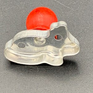 May include: A silver metal cookie cutter shaped like a fish with a red plastic handle.