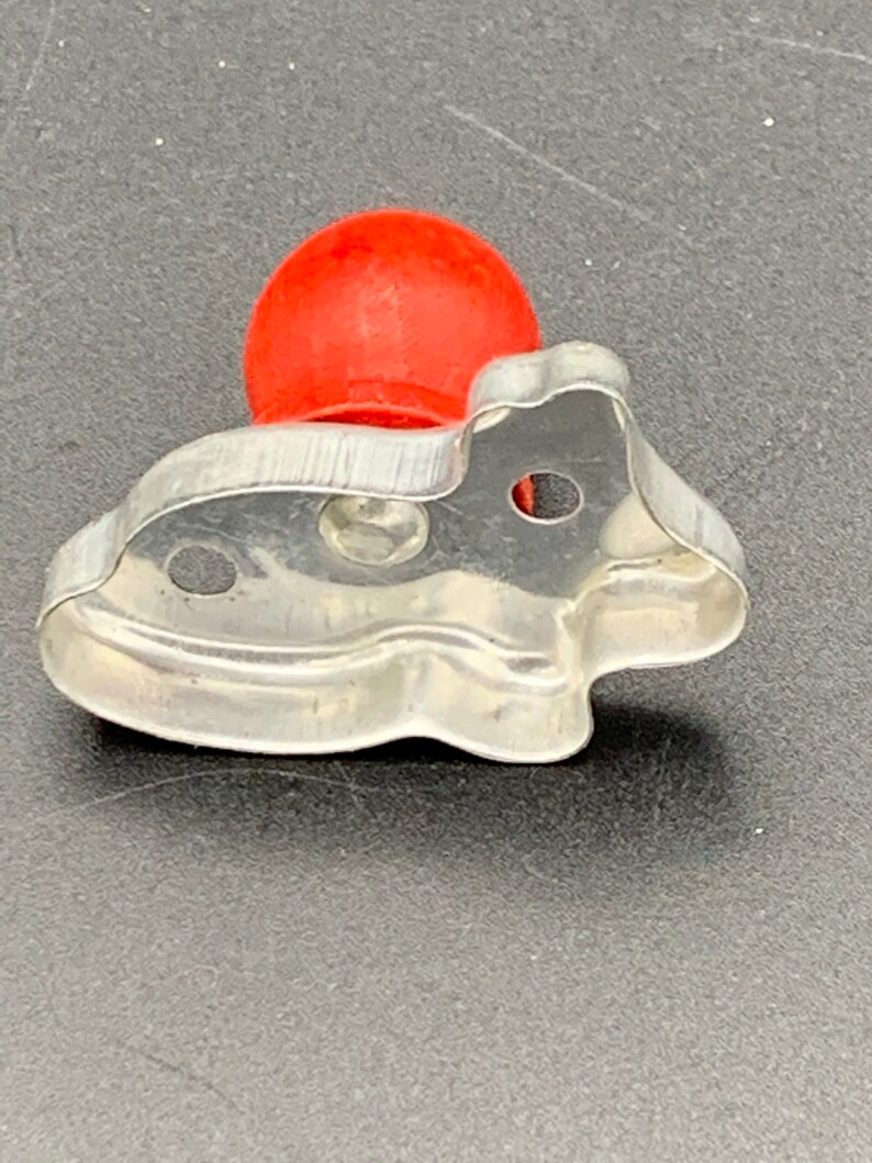 May include: A silver metal cookie cutter shaped like a fish with a red plastic handle.