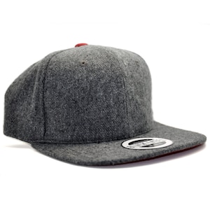 May include: A gray wool flat brimmed baseball cap with a red underside. The cap has a black label with the text "REYKJAVIK" in white.
