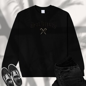 May include: Black sweatshirt with the word "Gothmas" embroidered in a gothic font, with two crossed candy canes. The sweatshirt is paired with black jeans and black and white sneakers.