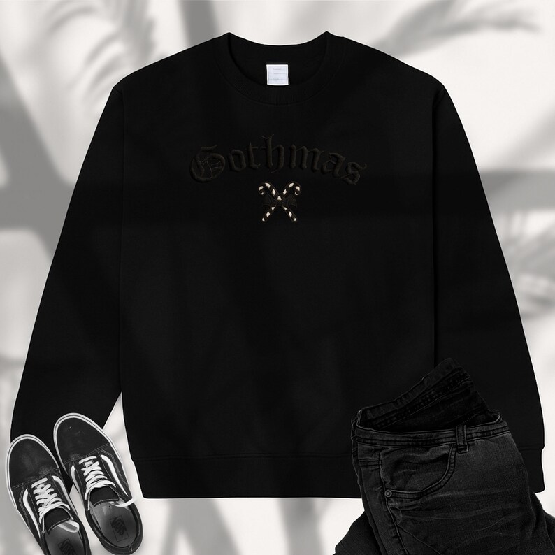 May include: Black sweatshirt with the word "Gothmas" embroidered in a gothic font, with two crossed candy canes. The sweatshirt is paired with black jeans and black and white sneakers.