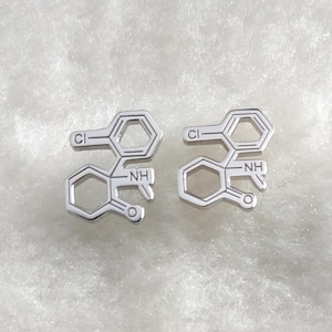 May include: A pair of silver earrings shaped like chemical structures with the text "Cl" and "NH" on them.