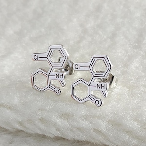 May include: A pair of silver stud earrings featuring a chemical structure design. The earrings are small and delicate, and they would make a great gift for a science enthusiast.