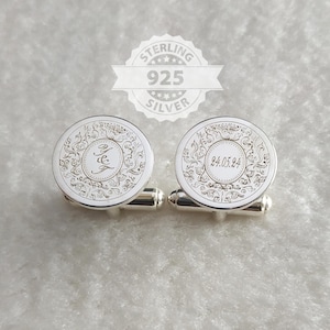 May include: A pair of round sterling silver cufflinks featuring an intricate engraved floral pattern. One cufflink displays the initials J&E in a script font, while the other shows the date 24.05.24. Both pieces have a polished metallic finish.